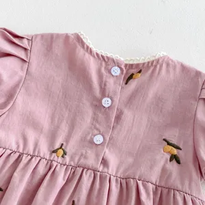 Primer plano detallado del hermoso vestido rosa de bebé con bordado de limón y botones.