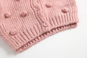 Close-up van roze gebreide baby vest trui met schattige pompons en knopen textuur detail.