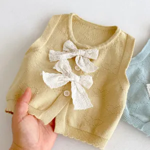 Dettaglio gilet neonato in maglia, dolce fiocco in pizzo, primo piano abbigliamento.