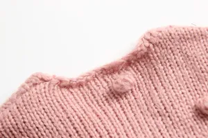 Detail opname roze gebreide baby trui, zachte wol textuur met handgemaakte bolletjes.