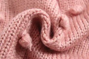 Detailopname van roze gebreid babyvest met handgemaakte pompons, zachte gebreide textuur.