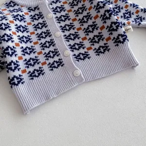 Close-up of infant knit cardigan sweater detail showing geometric nordic pattern and buttons.