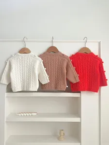 Gedetailleerd overzicht van babybreiwerk vesten met pompon en klassiek kabelpatroon.