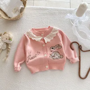 Close-up van roze gebreid babyvestje met witte kantkraag en schattige konijnenborduurwerkjes.
