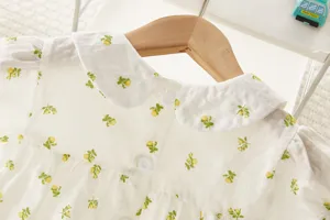 Detalle de blusa para bebé con estampado floral, cuello babero y botones traseros de estilo retro.