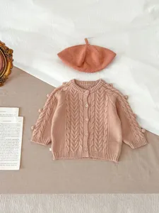 Detail van baby-breisel vest met kabelpatroon, schattige pompons en bijpassende baret.