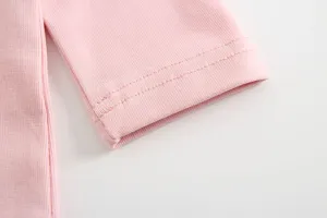 Dettaglio manica top in cotone per neonata rosa, tessuto morbido con cuciture pulite e design.