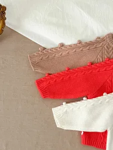 Gedetailleerd overzicht van baby kabelvest gebreide trui met schattige pompons.