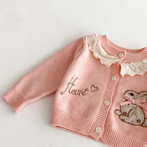 Detail van roze gebreid baby-meisjesvest met witte kanten kraag en schattig konijnenborduurwerk.