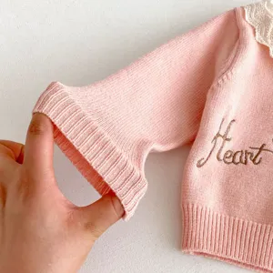 Close-updetail van de roze gebreide babyvestmouw, geribde manchet en fijne borduurwerkinformatie.