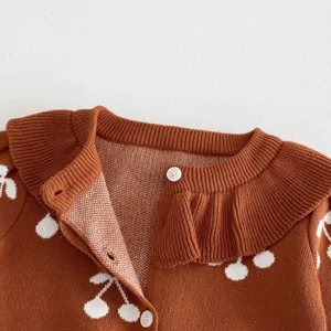 Close-up detail of infant baby girl brown knit cardigan sweater with white cherry print lapel.