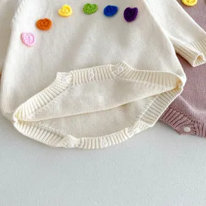 Vue détaillée d'une combinaison tricotée pour bébé avec des fleurs crochetées et boutons pression.