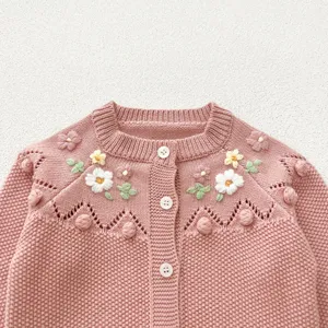 Baby girl knitted cardigan detail view with handmade floral embroidery and cute pom-poms.
