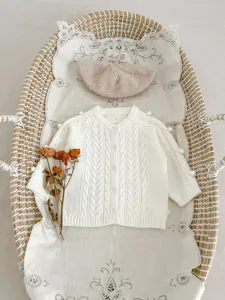 Schattige witte baby kabelbreisel cardigan trui met pompons en bijpassende baret plat gelegd.