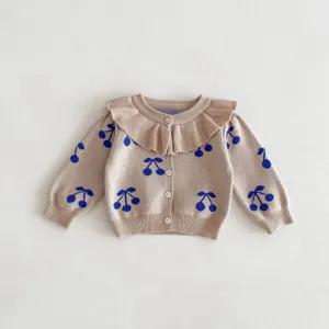 Detailed view of toddler girls knitted cardigan, beige sweater with blue cherry print, cute ruffles.