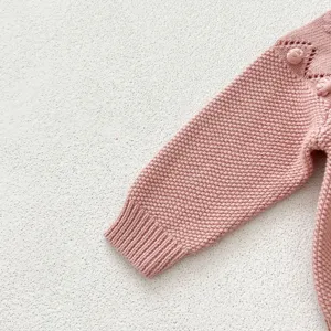 Baby girl knit sweater sleeve detail, cute pink chunky knit with textured pom-poms.