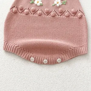 Close-up detail of cute pink knitted baby romper featuring embroidered daisy flowers and pom-poms.