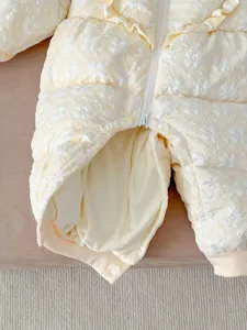Infant winter jumpsuit detail, light yellow floral jacquard fabric texture close-up.