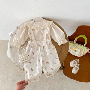 Vista dettagliata di camicetta in cotone per bambina e salopette con borse e scarpe coordinate.