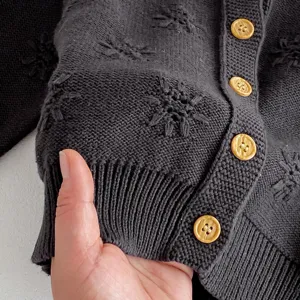 Baby Strickjacke Detail Nahaufnahme, weicher grauer Pullover mit goldenen Knöpfen.