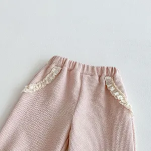 Pantaloni bimba in tessuto waffle rosa con delicate balze in pizzo bianco sulle tasche, dettaglio.