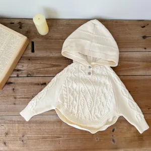 Detailed view of cozy cream knit hooded baby cape, featuring cable texture and front buttons.