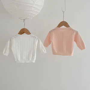 Primo piano dettagliato di cardigan in maglia per neonati appesi a grucce di legno.