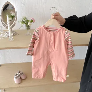 Detailed shot of cute baby girl pink striped top and overall set on hanger with shoes in room.