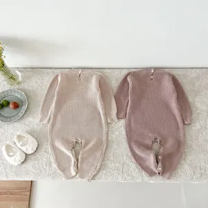 Detalle de mameluco tejido de bebé plano mostrando algodón beige y rosa suave