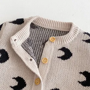 Baby knitted cardigan detail, beige cotton top featuring black moon print and natural wooden buttons.
