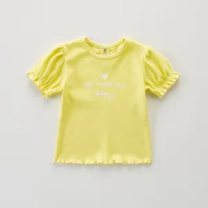 Vista detallada del top amarillo de manga corta para niñas con dobladillo ondulado y bordado.