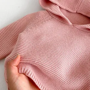 Close-up of pink baby knitted hoodie texture, showing soft wool detail and warm fabric weave.