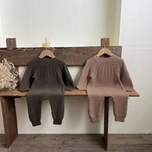 Detailed shot of two knitted baby rompers hanging on wooden hangers against a rustic bench backdrop.