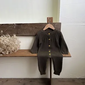 Detail view of a dark green knit baby romper, featuring a round neck and wooden buttons.