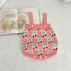Detailed shot of a cute pink checkered baby knitted romper featuring lovely cherry patterns and buttons.
