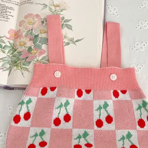 Baby knit romper detail shot showing cute pink checkered pattern and sweet cherry jacquard design.