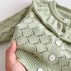 Close-up of infant knit cardigan showing hollow diamond pattern, large ruffled collar and buttons.
