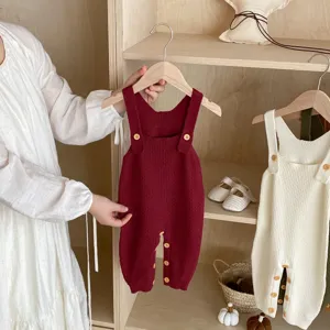 Baby knitted romper detail featuring cute wooden buttons and soft straps in cozy neutral tones.