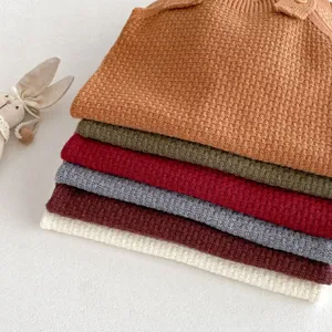 Detailed shot of stacked knitted baby rompers in multiple colors with cute bunny toy decor.