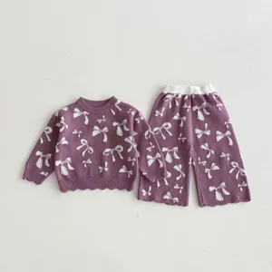 Girls knitwear detail showing jacquard bow pattern on purple sweater and pants set texture.