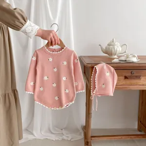 Primo piano dettagliato della graziosa tutina in maglia rosa con margherite ricamate.