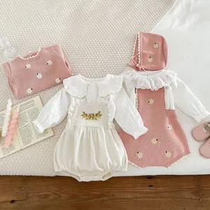Dettaglio maglione lavorato a maglia per neonati con ricamo floreale, tutina e accessori.