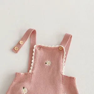 Primo piano del romper in maglia rosa per neonati con delicate margherite ricamate a mano.