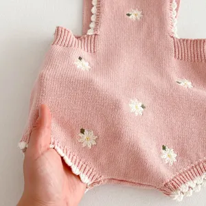 Dettaglio tutina neonata in maglia, cotone rosa con ricamo margherita bianca e bordo pizzo.