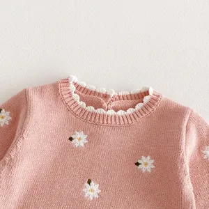 Dettaglio di maglione in maglia rosa per neonata con ricamo di margherite bianche e colletto.