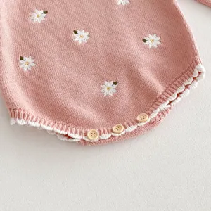 Primo piano di body neonato in maglia rosa con ricamo di margherite bianche.