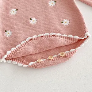 Primo piano di tutina in maglia per neonata rosa con ricamo floreale bianco e bottoni.