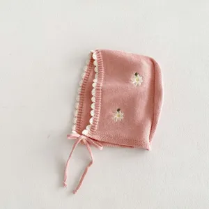 Dettaglio in primo piano del berretto rosa in maglia per neonati con bordo in pizzo e ricami.