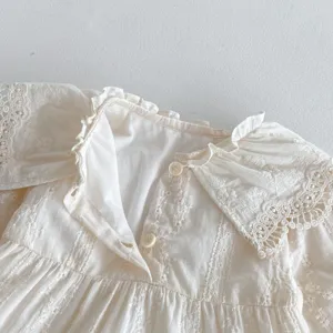 Vista dettagliata di un vestito beige da bambina con colletto in pizzo, ricami e bottoni.
