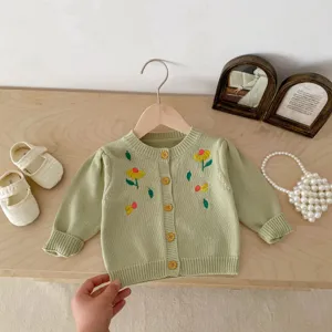 Detailed shot of baby knit cardigan with embroidered flowers and wooden buttons in soft green.